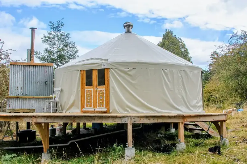 White yurt with a timber deck and glass doors in front of a forest